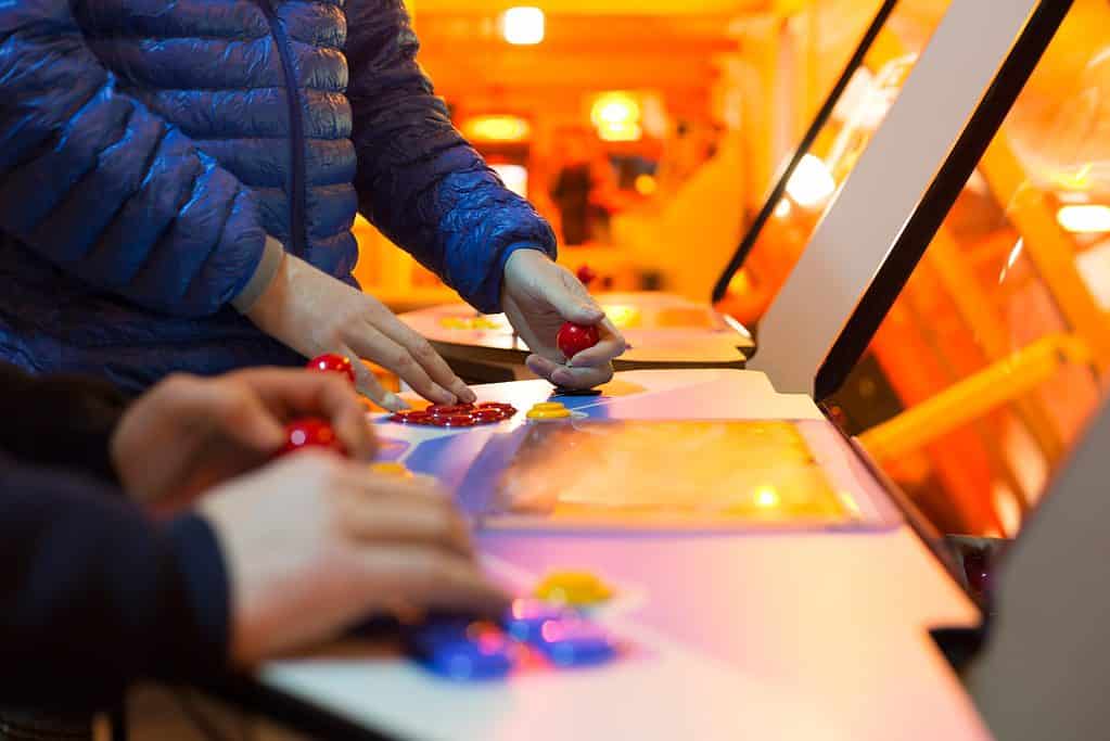 Detail of players hands interacting and playing with joysticks and buttons on an old arcade game in a gaming room